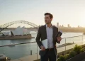 Jeune professionnel français travaillant sur un ordinateur portable avec la skyline de Melbourne en fond, illustrant le nouveau visa australie.