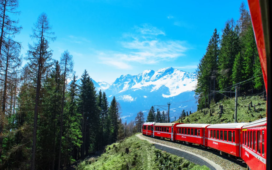 Vue sur les Alpes suisses depuis un train avec sommets enneigés et vallée verte